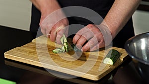 A man cutting a peeled cucumber on a wooden board. Art. Close up of male chef preparing a dish and using a steel knife