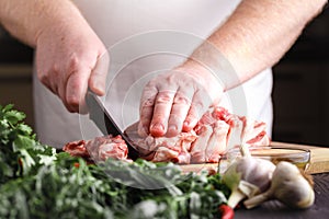 Man cutting rack of lamb on wooden board at restaurant kitchen. Chef preparing fresh meat for cooking