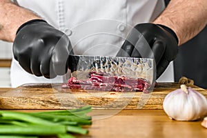 Man cutting raw beef meat. A chef in black gloves. Concept of cooking beef tartare