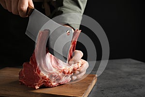Man cutting raw ribs at grey table, closeup. Space for text