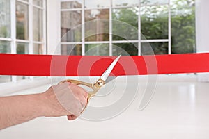 Man cutting red ribbon on blurred background.