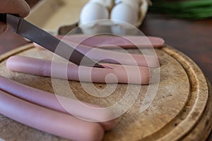 A man is cutting a sausage with a knife. An adult male cuts along a sausage on a cutting board. Cooking a meal. Selection trick