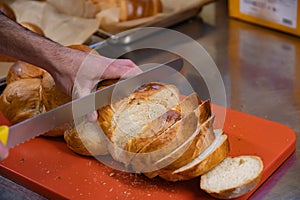 Man cutting slicing a loft of fresh swiss zopf braided bread with a serrated knife