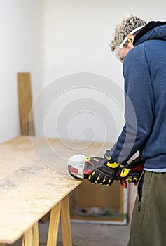 Man cutting wood with electric saw wearing protective gloves and glasses at home