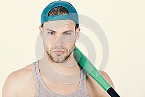 Man in cyan green baseball hat on white background. Guy in grey tank top holds bright green bat.