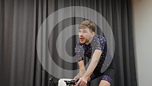 Man cycle out of saddle and drinking isotonic while hard training on smart bicycle trainer. Indoor cycling virtual concept. Male d