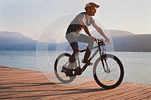 Man cycling on bicycle near beautiful mountain lake, leisure biking