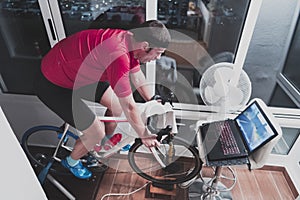 Man cycling on the machine trainer he is exercising in the home at night playing online bike racing game