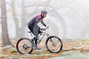 Man cycling with mountain bike in a forest with fog in the background