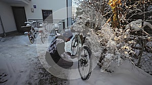 Man cyclist brushes his bicycle in the backyard in winter before taking it into the parking garage. Winter cycling and