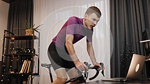 Man cyclist is cycling on indoor smart bike trainer. Male triathlete is training on stationary bicycle at home during coronavirus