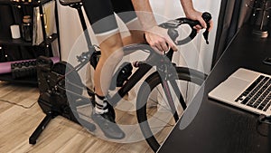 Man cyclist is exercising at home by cycling on indoor smart trainer. Male athlete is training with stationary bicycle. Fitness sp