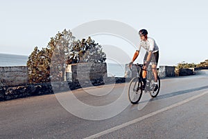 Man cyclist pedaling on a road bike outdoors in sun set