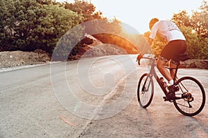 Man cyclist pedaling on a road bike outdoors in sun set