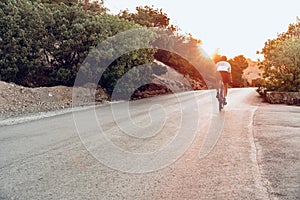 Man cyclist pedaling on a road bike outdoors in sun set