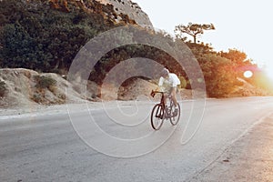 Man cyclist pedaling on a road bike outdoors in sun set