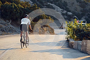 Man cyclist pedaling on a road bike outdoors in sun set