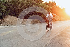 Man cyclist pedaling on a road bike outdoors in sun set