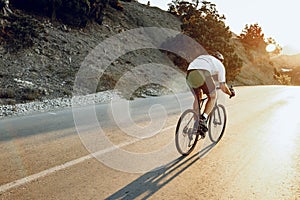 Man cyclist pedaling on a road bike outdoors in sun set