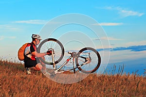 Man cyclist repairing a bike against blue sky