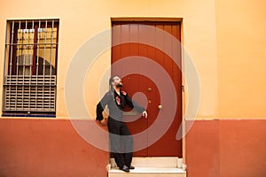 Man dancing flamenco with black shirt and red roses, on the background of a red wooden door, he is waiting leaning on the door.