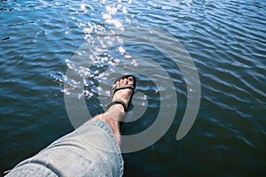The man dangled his feet in sandals sitting by the water