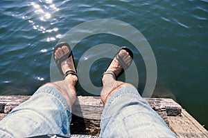 The man dangled his feet in sandals sitting by the water