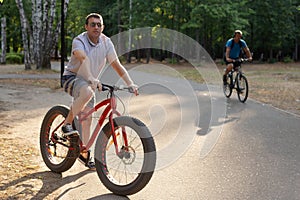 A man in dark glasses rides a bicycle in a public park in the summer. Sports and leisure