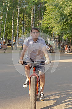 A man in dark glasses rides a bicycle in a public park in the summer. Sports and leisure