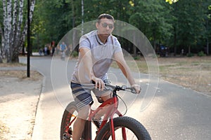 A man in dark glasses rides a bicycle in a public park in the summer. Sports and leisure