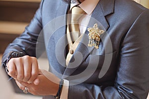 Man in dark grey suit two bottons golden star brooch, checking whatch, close up photo