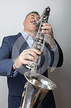 A man, dark, short hair, plays the bass clarinet. Studio, light background
