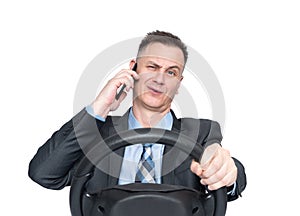 A man in a dark suit and tie talks on a smartphone and holds a car steering wheel in his hand, isolated on white background.