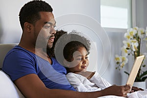 Man and daughter sitting in bed watching computer, waist up