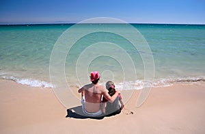 Man and daughter sitting on sunny deserted beach