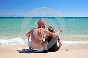 Man and daughter sitting on sunny deserted beach