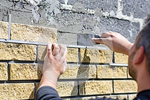 Man decorates the facade of the fence with decorative torn bricks, close up. Work at home during quarantine. Do it yourself