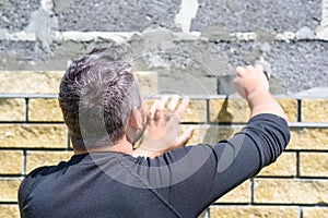 Man decorates the facade of the fence with decorative torn bricks. Work at home during quarantine. Do it yourself