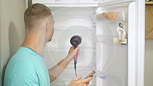 A man defrost the refrigerator with a hairdryer. adventures of strange people