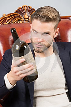 Man degustator with beard, stylish hair hold wine bottle