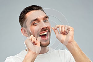 Man with dental floss cleaning teeth over gray