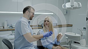 Man dentist shows patient girl how to properly brush her teeth in dental office. Dentist and patient talking about teeth