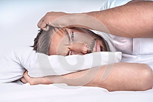 Man with depressive disorder lying on the pillow in the bed. Depressed man with negative thoughts.