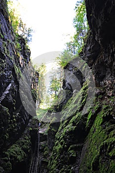 A man descends a steep iron staircase down among the rocks covered with green moss.