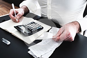 Man at desk with calculator, bills or sales slips and notpad