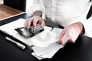 Man at desk with calculator, bills or sales slips and notpad