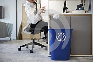 Man at desk throwing screwed up paper into recycling bin