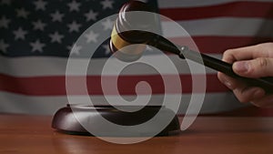 Man at the desk with wooden hammer and USA flag at the background. Judge in the court room, hitting wooden gavel, close