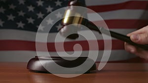 Man at the desk with wooden hammer and USA flag at the background. Judge in the court room, hitting wooden gavel, close