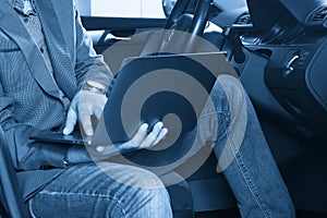 Man diagnosing car with computer sitting on the driver seat at the car service